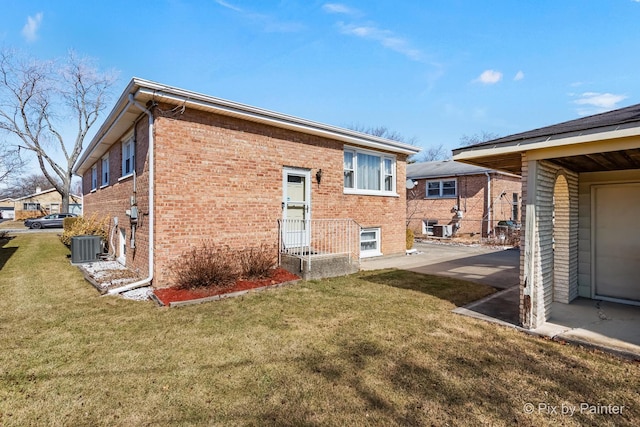 back of property featuring cooling unit, brick siding, and a yard