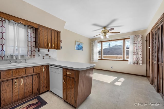 kitchen with white dishwasher, a peninsula, a sink, light countertops, and decorative backsplash