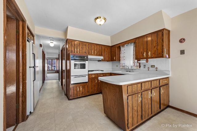 kitchen with a warming drawer, decorative backsplash, a peninsula, white appliances, and under cabinet range hood