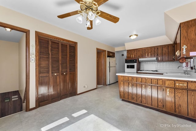 kitchen featuring under cabinet range hood, white appliances, a sink, light countertops, and backsplash