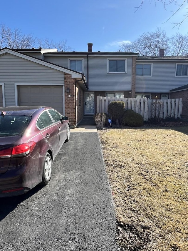 view of front of property featuring brick siding, fence, driveway, and an attached garage