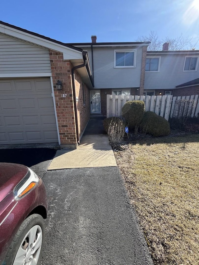 view of front of house with a garage, fence, aphalt driveway, and brick siding