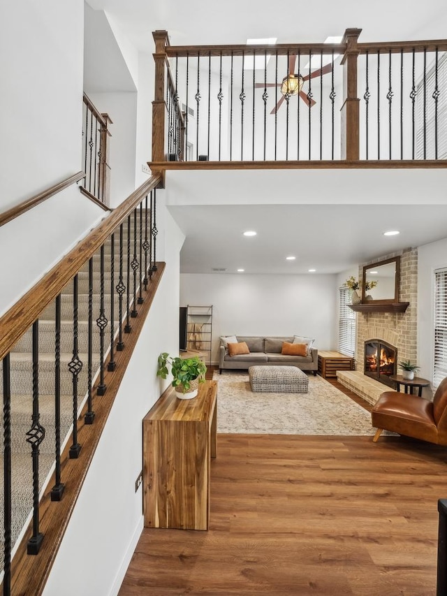 living room with stairs, a brick fireplace, wood finished floors, and a towering ceiling