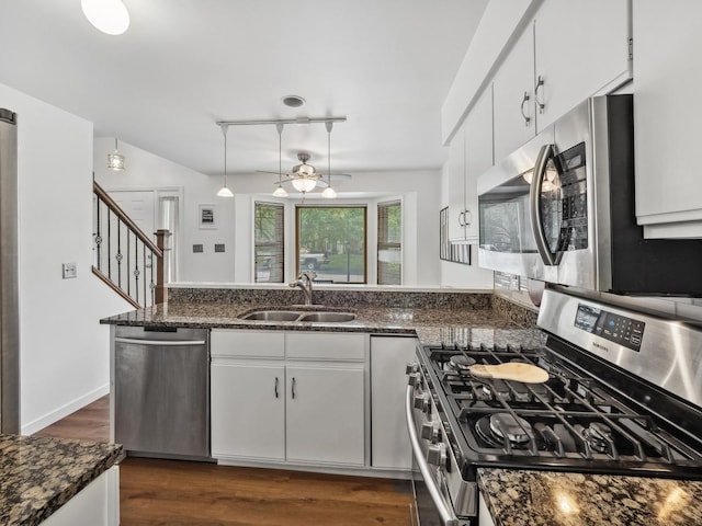 kitchen with a sink, a peninsula, white cabinets, stainless steel appliances, and dark wood-style flooring