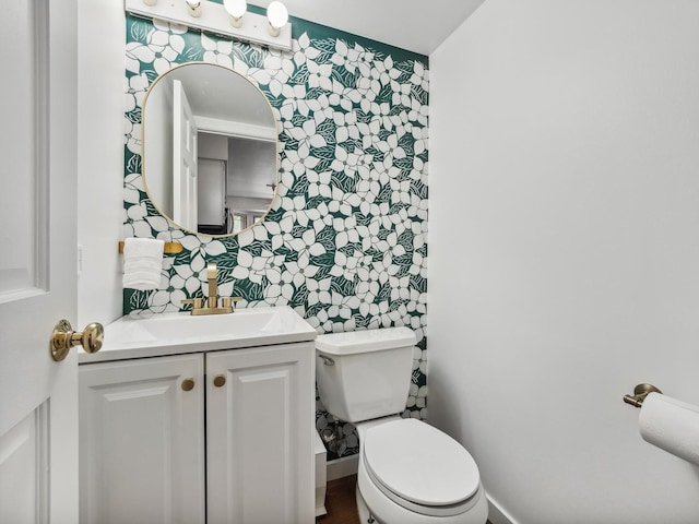 half bath with wallpapered walls, toilet, vanity, and baseboards