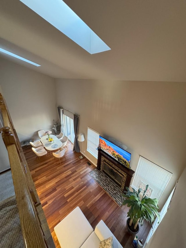 unfurnished living room with wood finished floors, lofted ceiling with skylight, and a fireplace with flush hearth