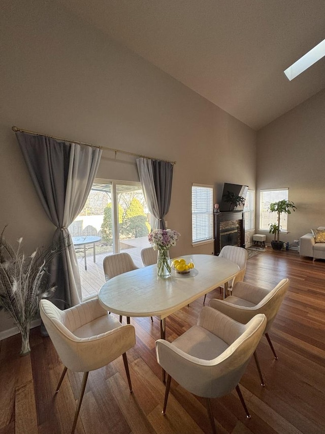 dining room featuring a skylight, baseboards, a glass covered fireplace, wood finished floors, and high vaulted ceiling