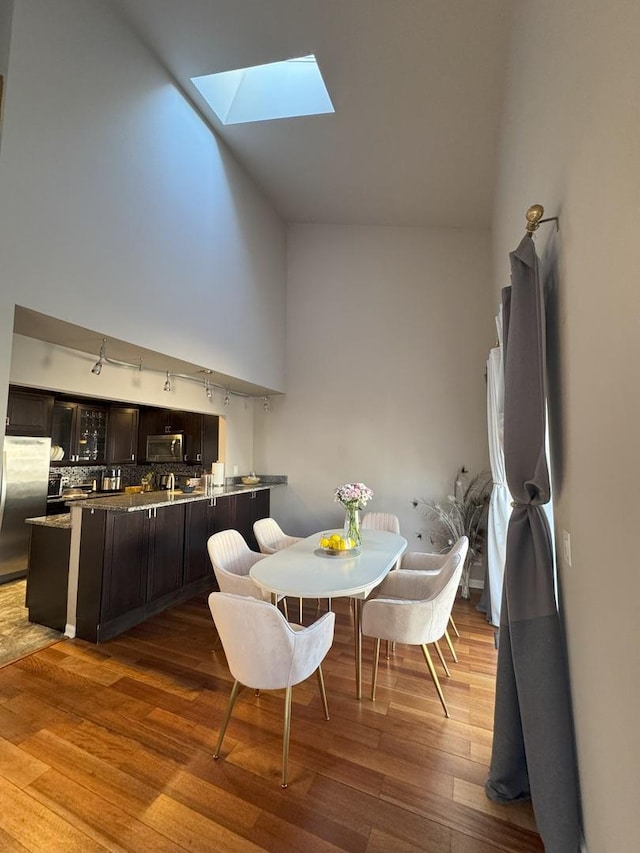 dining room featuring a towering ceiling, a skylight, and wood finished floors