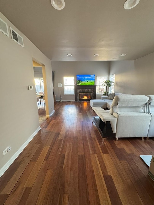 living room with dark wood-style floors, a glass covered fireplace, visible vents, and baseboards