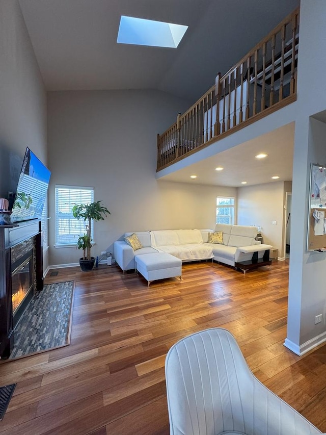 living area with a healthy amount of sunlight, high vaulted ceiling, wood finished floors, and a glass covered fireplace