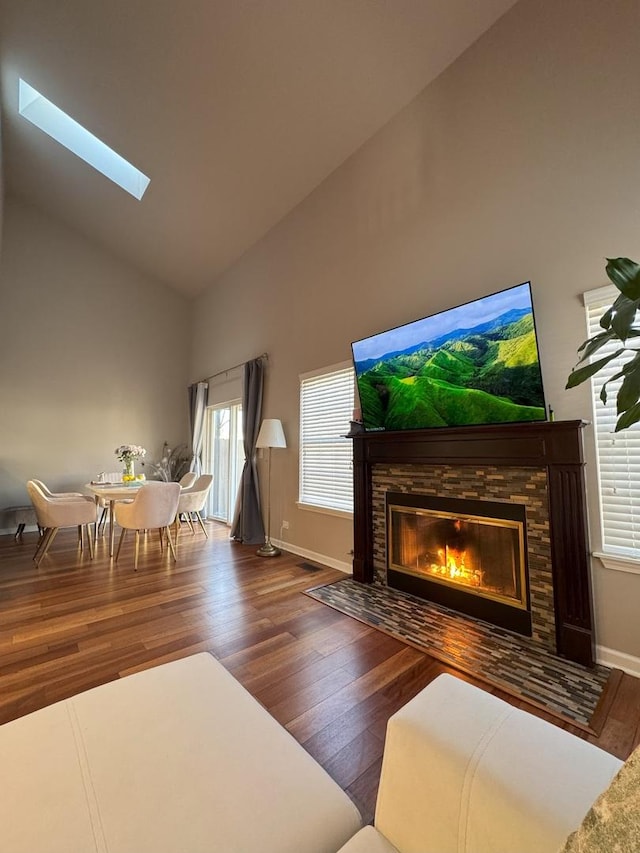 unfurnished living room featuring a skylight, baseboards, wood finished floors, a stone fireplace, and high vaulted ceiling