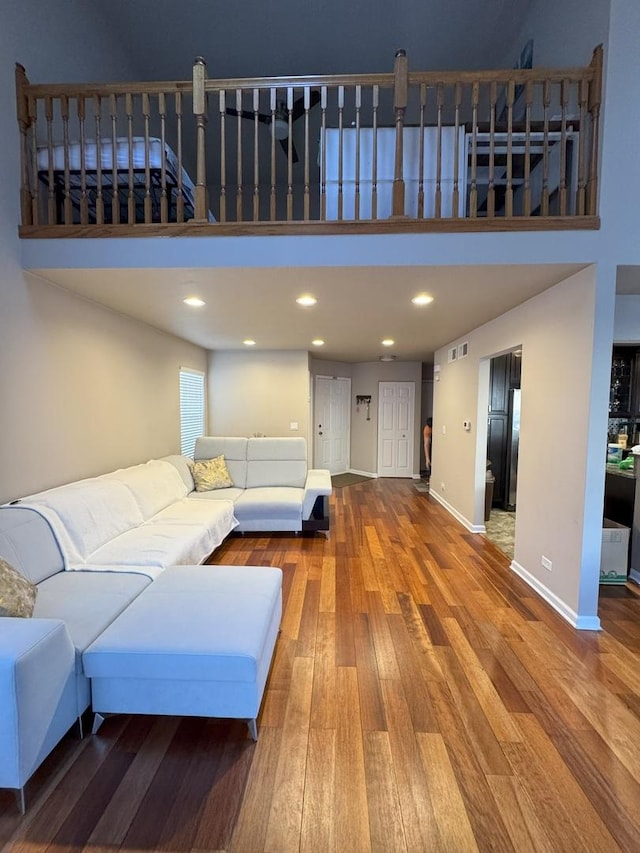 unfurnished living room featuring recessed lighting, visible vents, a high ceiling, baseboards, and hardwood / wood-style flooring