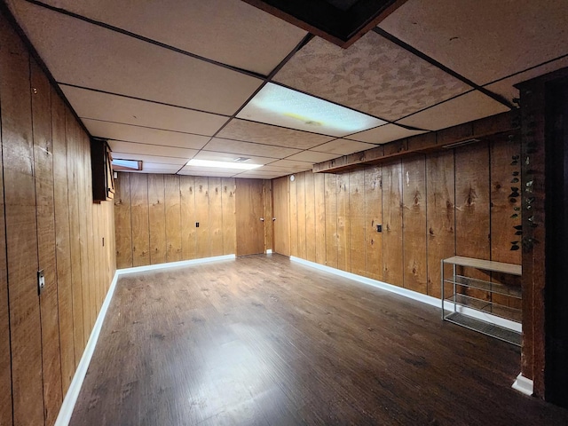 finished below grade area with a paneled ceiling, wooden walls, baseboards, and wood finished floors