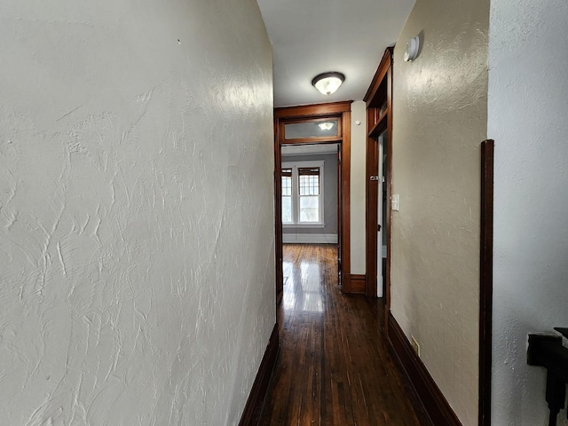 corridor featuring dark wood-style floors, a textured wall, and baseboards