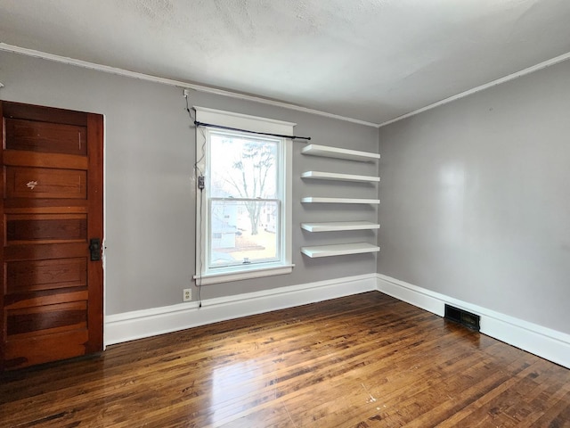 spare room with wood-type flooring, visible vents, crown molding, and baseboards