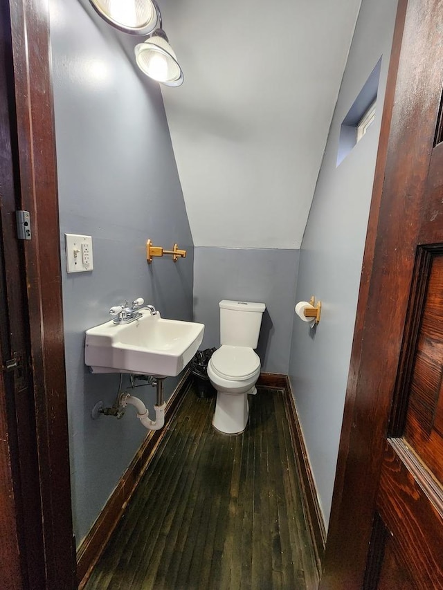 bathroom with baseboards, toilet, hardwood / wood-style flooring, vaulted ceiling, and a sink