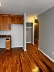 kitchen with dark wood-style flooring, brown cabinetry, and baseboards