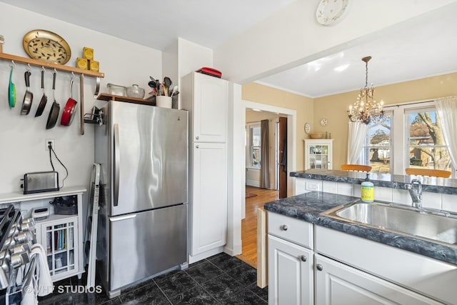 kitchen featuring dark countertops, white cabinetry, freestanding refrigerator, and a sink