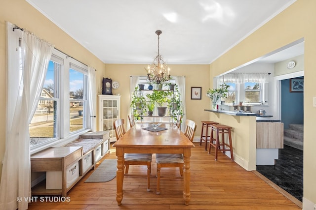 dining area with light wood-type flooring, ornamental molding, baseboards, a chandelier, and stairs