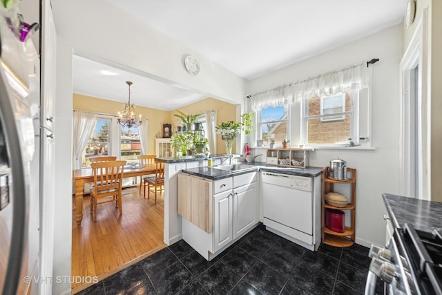 kitchen featuring a notable chandelier, pendant lighting, dark countertops, stainless steel appliances, and a peninsula