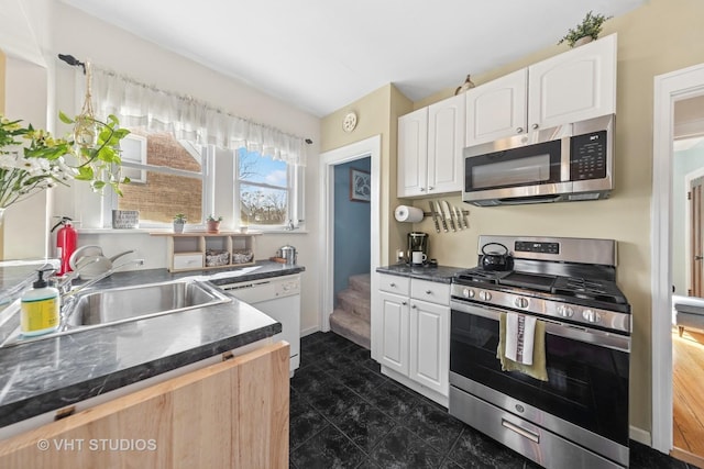 kitchen featuring dark countertops, baseboards, white cabinets, stainless steel appliances, and a sink