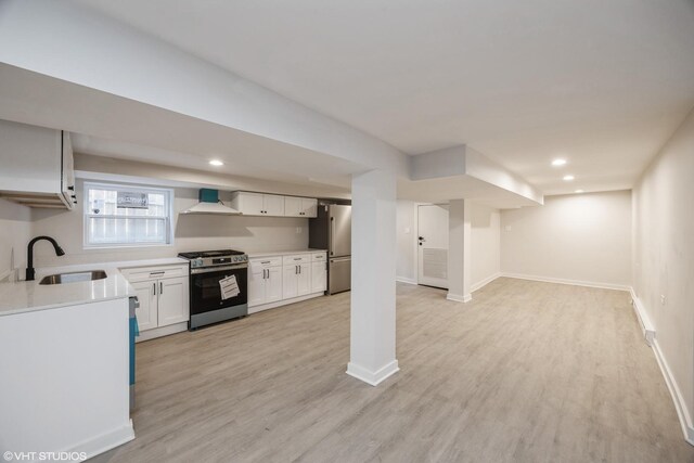 kitchen featuring stainless steel appliances, light countertops, light wood-style floors, a sink, and wall chimney exhaust hood