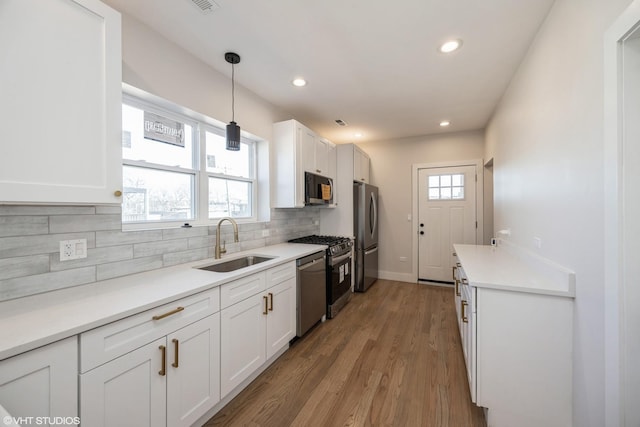 kitchen with tasteful backsplash, appliances with stainless steel finishes, white cabinets, a sink, and wood finished floors