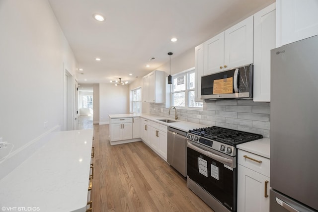 kitchen with light countertops, backsplash, appliances with stainless steel finishes, white cabinets, and a sink