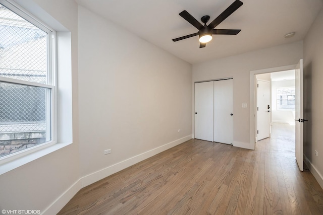 unfurnished bedroom with light wood-type flooring, a closet, multiple windows, and baseboards