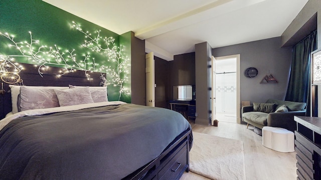 bedroom featuring an accent wall, light wood-type flooring, ensuite bath, and beam ceiling