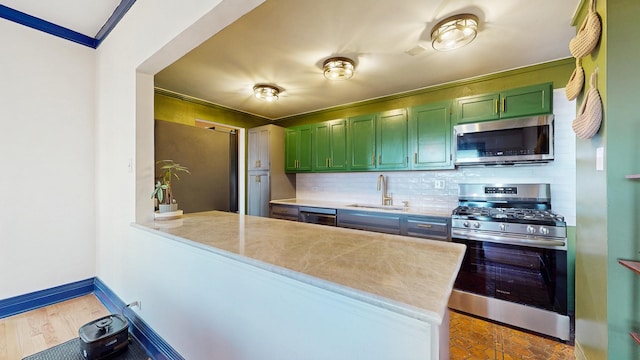 kitchen featuring stainless steel appliances, a sink, baseboards, tasteful backsplash, and green cabinetry