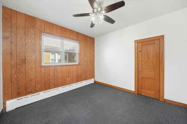 empty room with carpet floors, baseboard heating, wooden walls, a textured ceiling, and baseboards