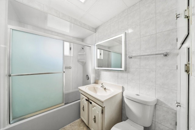 full bathroom featuring toilet, shower / bath combination with glass door, vanity, and tile walls