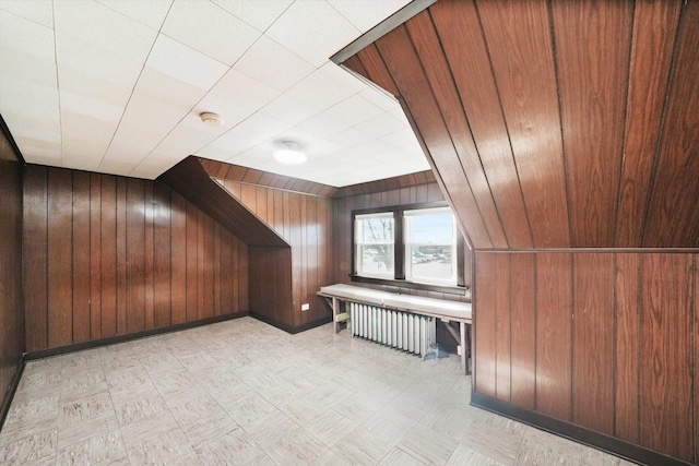 bonus room with light floors, baseboards, wood walls, and radiator heating unit