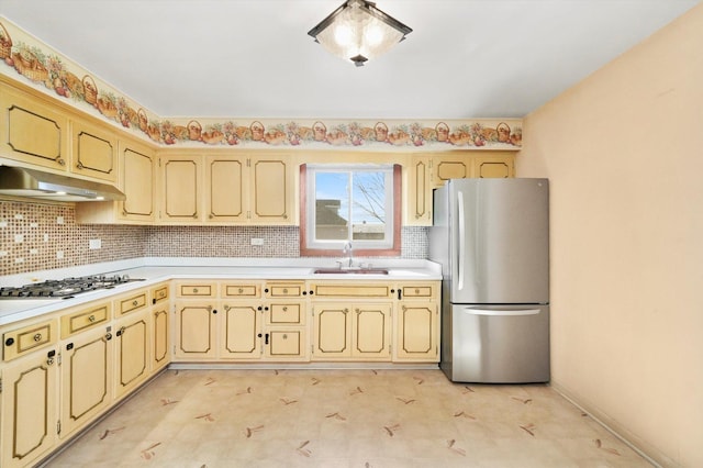 kitchen with white gas stovetop, freestanding refrigerator, light countertops, under cabinet range hood, and a sink