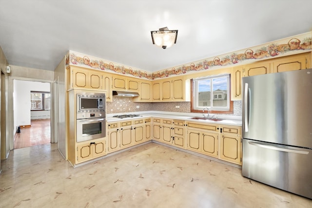 kitchen with stainless steel appliances, tasteful backsplash, light countertops, a sink, and under cabinet range hood