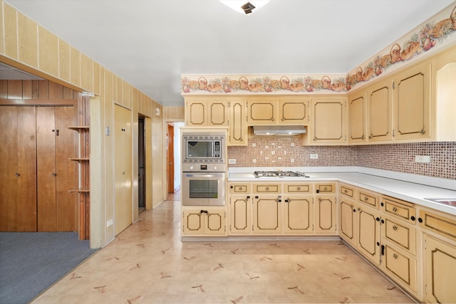 kitchen with decorative backsplash, cream cabinets, stainless steel appliances, light countertops, and under cabinet range hood