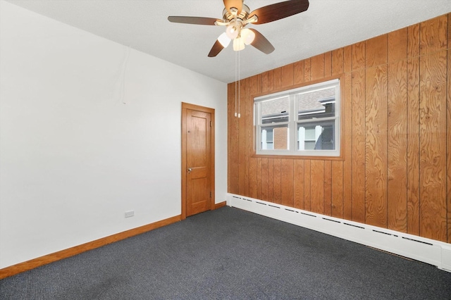 empty room featuring ceiling fan, wooden walls, baseboards, baseboard heating, and dark colored carpet