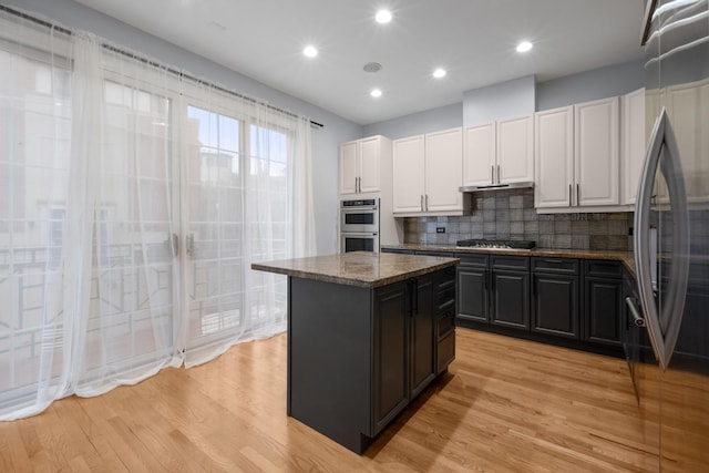 kitchen with a center island, decorative backsplash, appliances with stainless steel finishes, white cabinetry, and light wood-type flooring