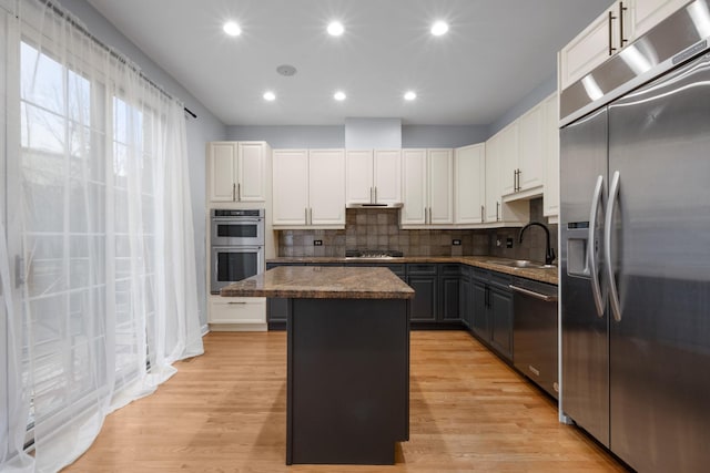 kitchen featuring a center island, light wood finished floors, stainless steel appliances, white cabinets, and a sink