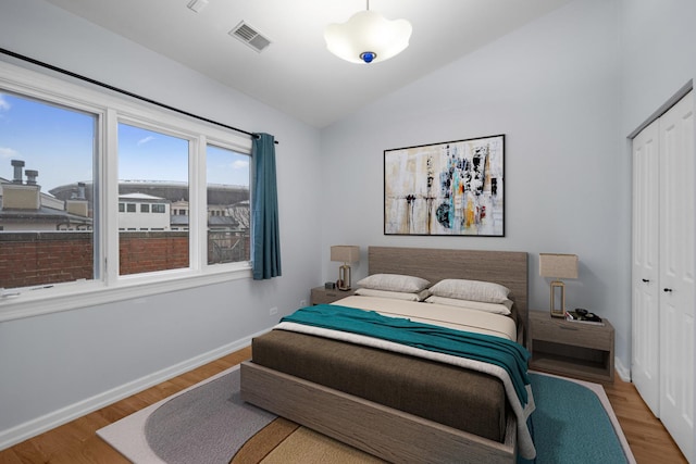 bedroom featuring lofted ceiling, a closet, visible vents, and wood finished floors