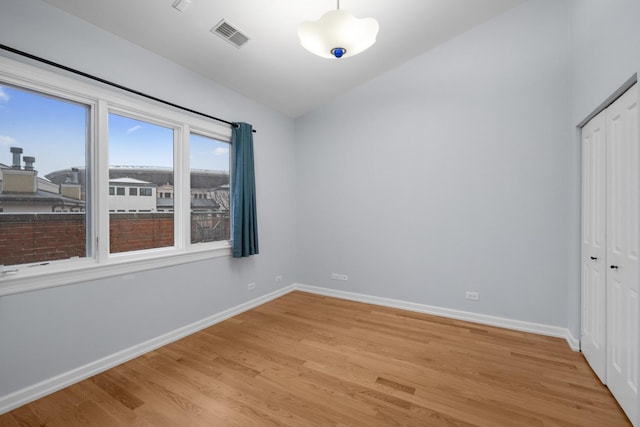 unfurnished bedroom featuring lofted ceiling, visible vents, baseboards, light wood-style floors, and a closet