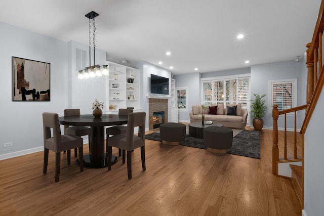 dining room featuring recessed lighting, stairway, wood finished floors, and a glass covered fireplace