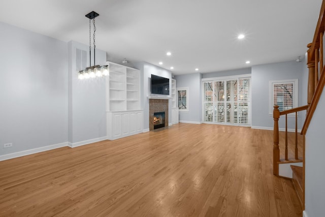 unfurnished living room with light wood-type flooring, a fireplace with flush hearth, stairs, and recessed lighting