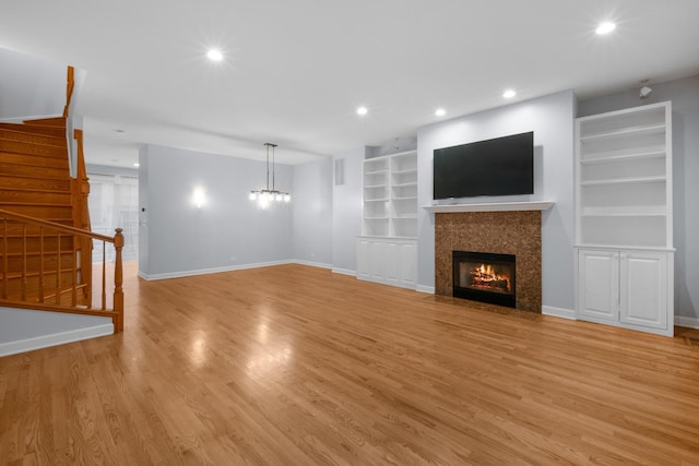 unfurnished living room featuring built in features, light wood-style flooring, stairway, a fireplace with flush hearth, and baseboards