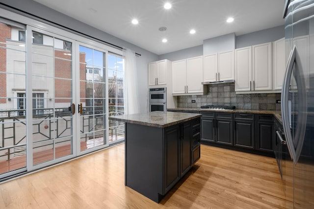 kitchen featuring stainless steel appliances, backsplash, light wood-style flooring, white cabinets, and a kitchen island