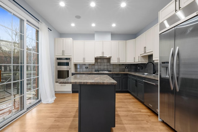 kitchen with a sink, a kitchen island, white cabinetry, light wood-style floors, and appliances with stainless steel finishes