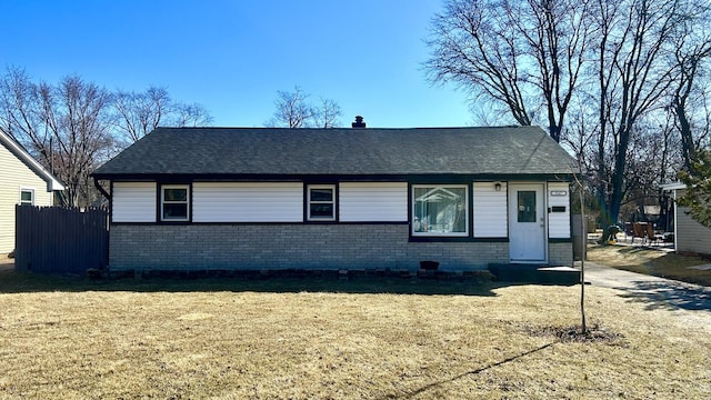 view of front of home featuring a shingled roof, brick siding, fence, and a front lawn