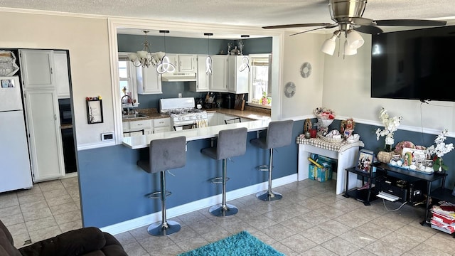 kitchen with white appliances, a peninsula, under cabinet range hood, a kitchen bar, and white cabinetry