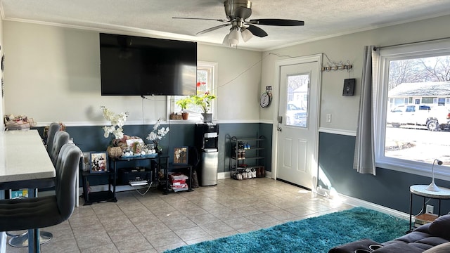 tiled living area with a ceiling fan, plenty of natural light, ornamental molding, and a textured ceiling